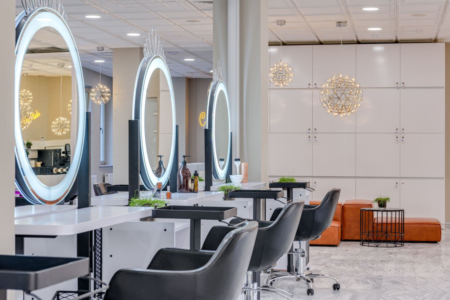 A salon before opening: a row of styling chairs facing lit round mirrors, every station empty and set.